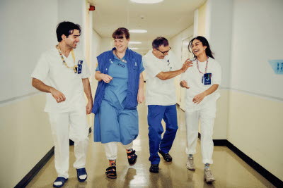 Fyra skrattande kollegor i en korridor. Glädje, flams, gemenskap.