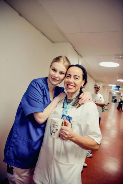 Två glada kvinnliga kollegor som håller om varandra i en korridor under en paus. Omtanke, glädje, gemenskap.