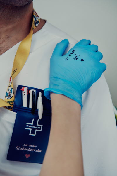 Handskbeklädd hand med texten "Vi fixar det! på kollegans axel. Omtanke, gemenskap.