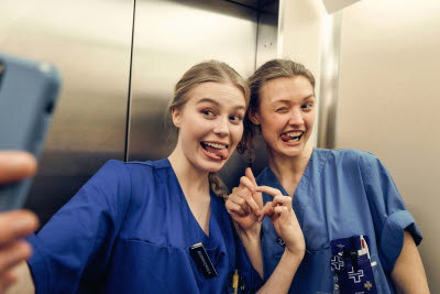 Två kvinnor flamsar och tar en selfie i hissen. Glädje, gemenskap och flams.