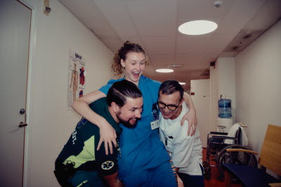 Skrattande kollegor i en korridor som busar med varandra. Två personer lyfter en tredje. Glädje, gemenskap och flams.