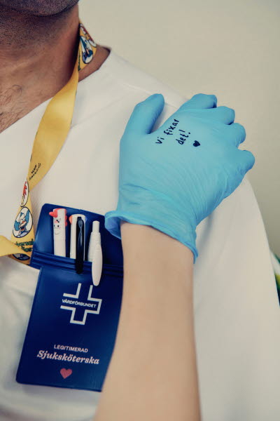 Handskbeklädd hand med texten "Vi fixar det! på kollegans axel. Omtanke, gemenskap.