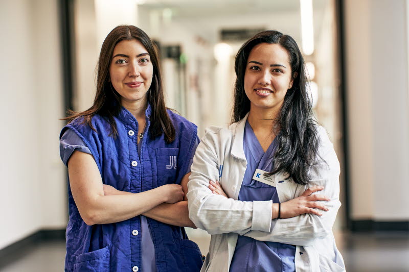 Biomedicinsk analytiker, klinisk fysiologi, två leende kvinnor med armarna i kors i korridor, Karolinska sjukhuset i Solna
