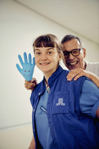 Två skrattande kollegor och en uppblåst handske med en smiley på. Gemenskap, flams, glädje.