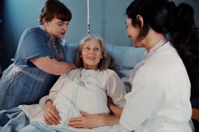 Sjuksköterskor sköter om glad patient i vårdsäng.