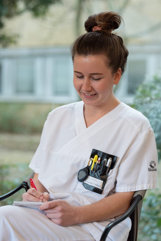 Lina Nilsson, sjuksköterska, sitter och antecknar i ett block, leende, Centralsjukhuset Kristianstad. Årsberättelse 2021.
