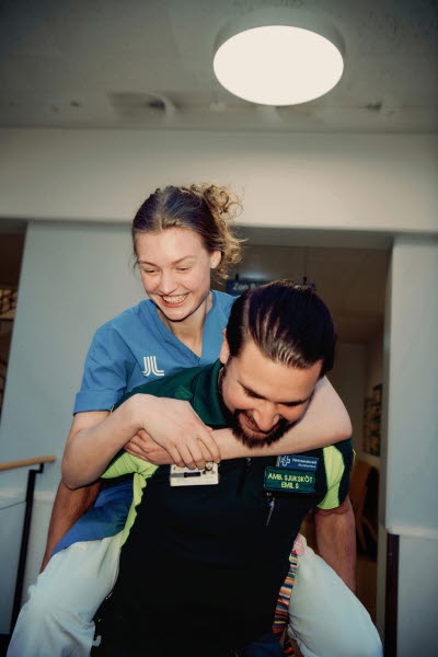 Skrattande vinna som bärs på manlig kollegas rygg. Sjuksköterska, ambulans, glädje, frams och gemenskap