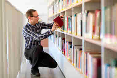 Student letar bok bland hyllorna på ett bibliotek.