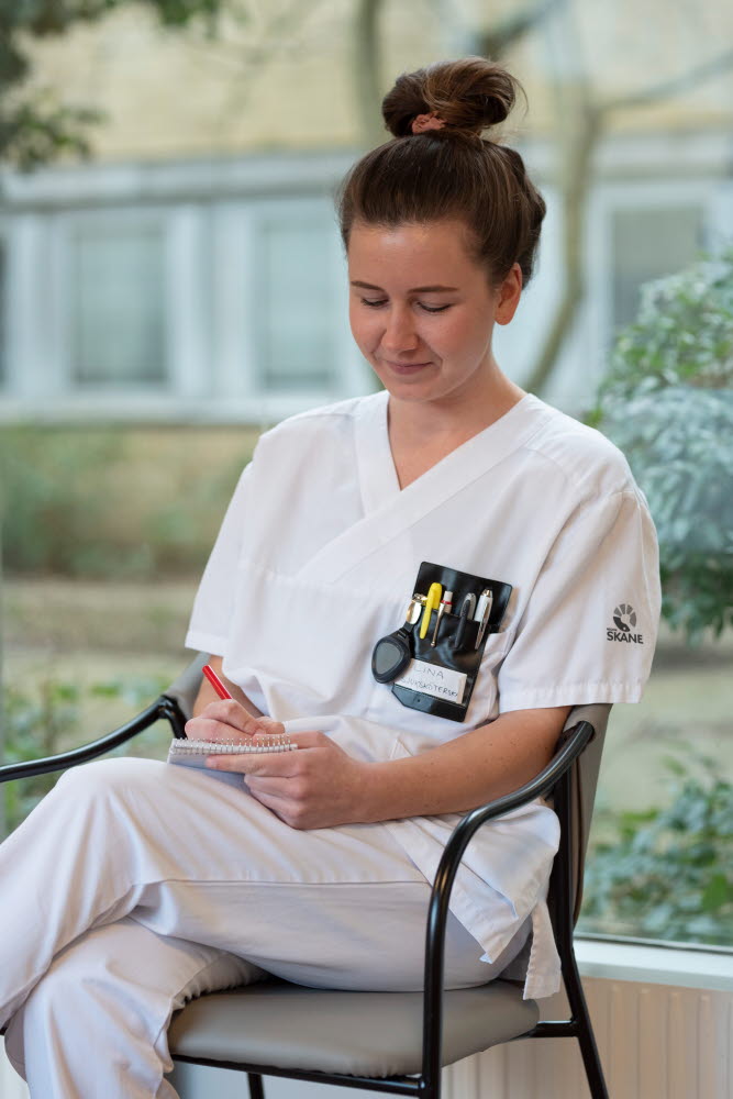 Lina Nilsson, sjuksköterska,sitter och antecknar i ett block, allvarlig, Centralsjukhuset Kristianstad. Årsberättelse 2021.