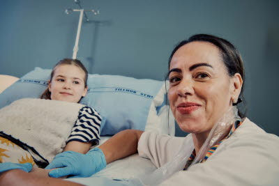 Sjuksköterska med en flicka som ligger på en vårdsäng i bakgrunden.