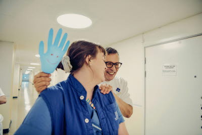 Två skrattande kollegor och en uppblåst handske med en smiley på. Gemenskap, flams, glädje.