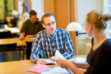 Student sitter vid ett bord på bibliotek tillsammans med en annan student