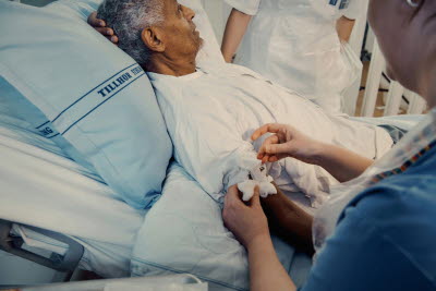 Sjuksköterska sköter om patient i vårdsäng.