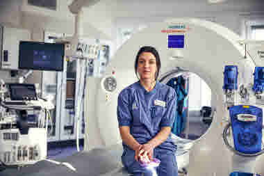 Allvarlig röntgensjuksköterska sittande på britsen framför röntgen. Danderyds sjukhus, röntgen. Oktober 2021.