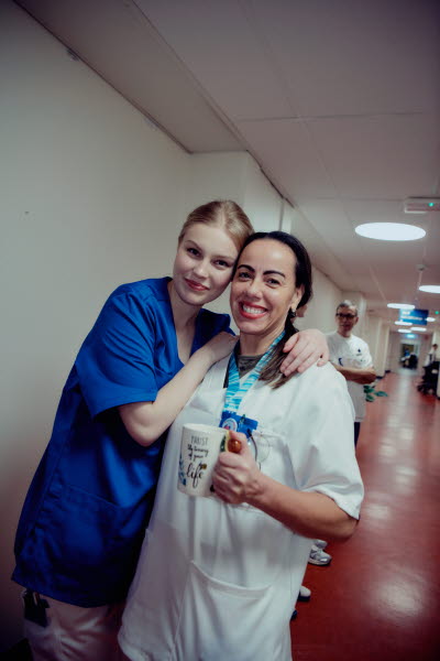 Två glada kvinnliga kollegor som håller om varandra i en korridor under en paus. Omtanke, glädje, gemenskap.