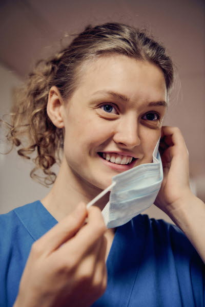 Leende ung kvinna som är på väg att sätta på sig ett munskydd. Glädje, personlighet