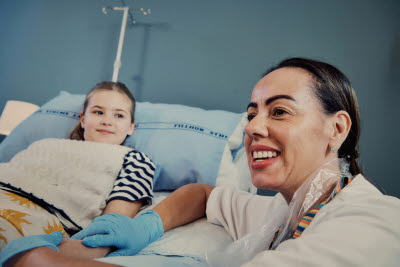 Glad sjuksköterska med en flicka som ligger på en vårdsäng i bakgrunden.