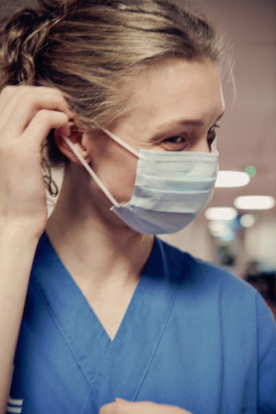 Leende ung kvinna som sätter på sig ett munskydd. Glädje, personlighet