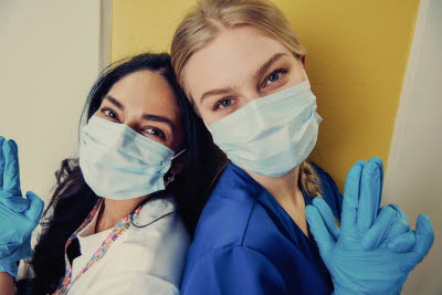 Två kvinnor med munskydd står med ryggen mot varandra och lutar sig mot varandra. Gemenskap, glädje

OBS beskär bort händerna vid användning