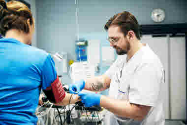 Biomedicinsk analytiker fäster elektroder på patient som sitter på testcykel, klinisk fysiologi, arbets-EKG, man, Karolinska sjukhuset i Solna