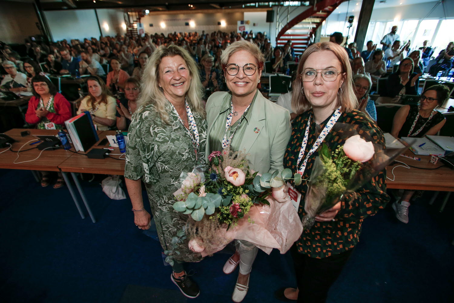 Kongress 2022, val av förbundsstyrelse, nya presidiet, ordförande, vice ordförande, framför kongressombuden i salen. Janí Stjernström, Sineva Ribero, Madeleine Meramveliotaki.