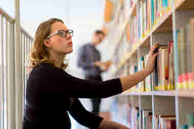 Student letar bok bland hyllorna på ett bibliotek.