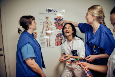 Skrattande kollegor i en korridor vid en plansch som visar hjärtat. gemenskap, glädje, flams.