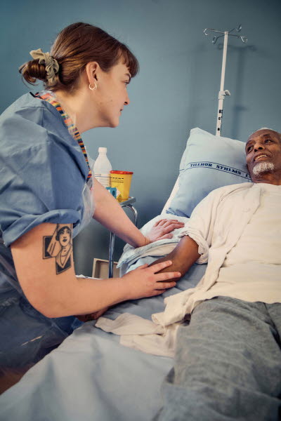 Sjuksköterska lyssnar till patienten i vårdsängen.