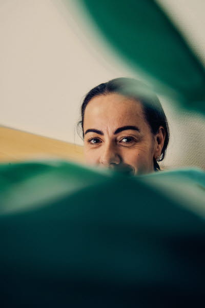 Kvinna med leende ögon skymtar bakom en grön växt. Personlighet glädje.