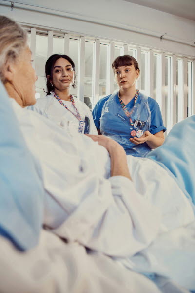 Sjuksköterskor i samtal med patient i vårdsäng.